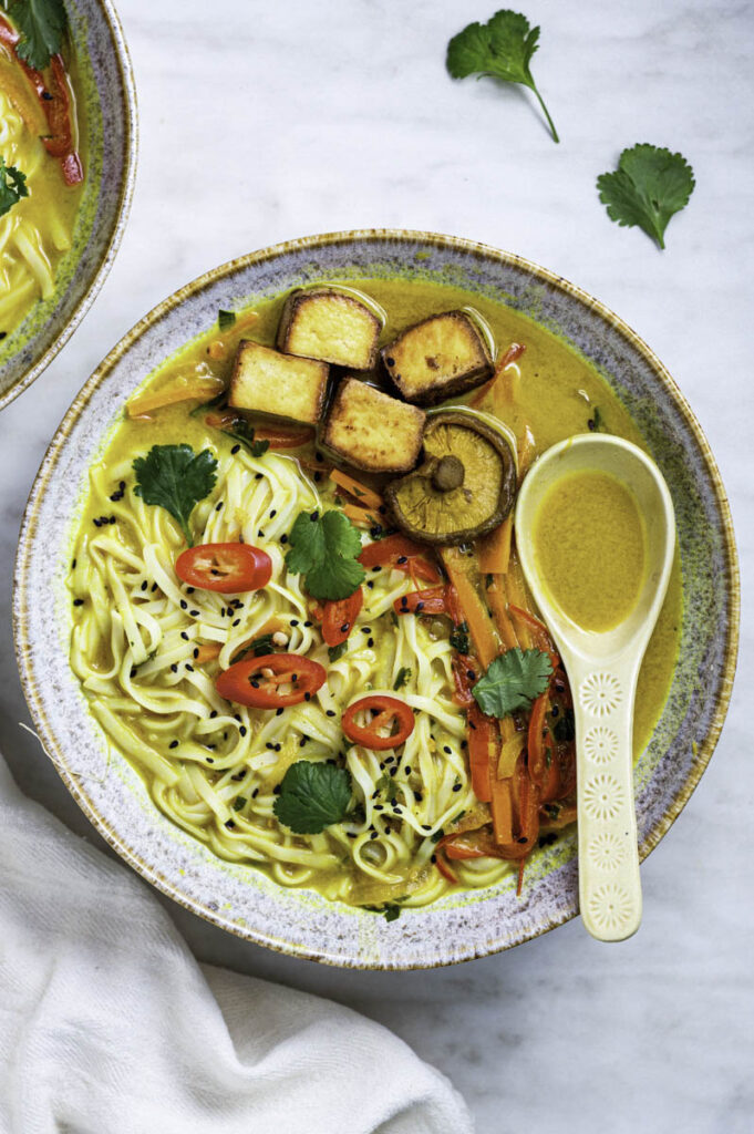 Vegan noodle soup served in a blue bowl with a spoon it.