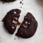 A chocolate cookie broken in two with melty chocolate in the middle, topped with flaky sea salt.