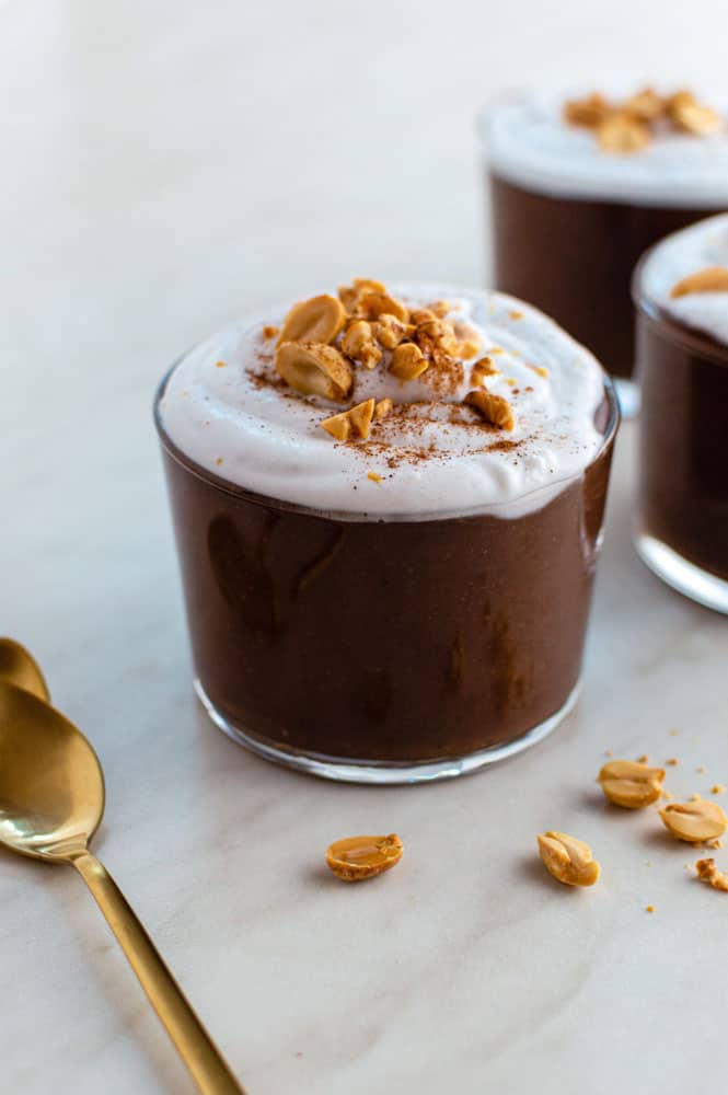 Chocolate peanut butter pudding served in a glass cup, and topped with whipped cream and crushed peanuts.