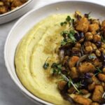 Vegan polenta served in a white plate and topped with roasted vegetables and micro greens.
