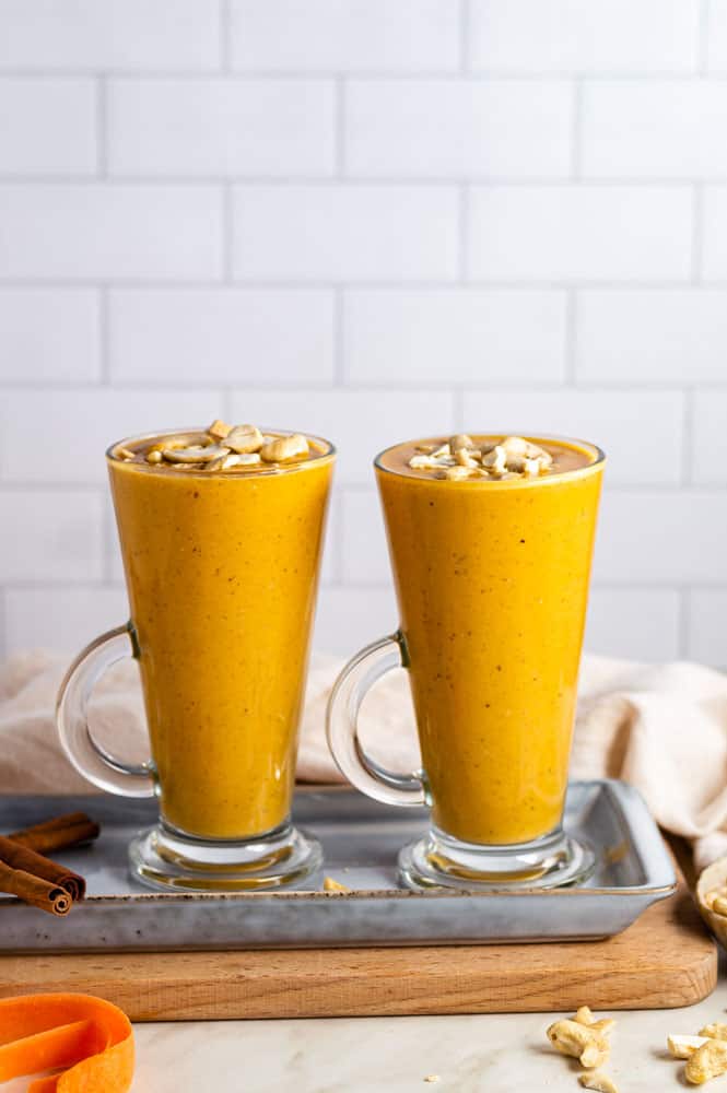 Two glasses filled with carrot banana smoothie and topped with chopped cashew nuts.