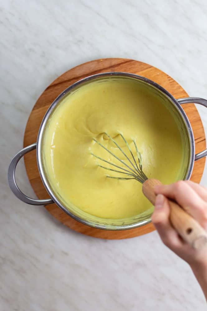 A hand mixing vegan lemon filling with a whisk from a stainless-steel pot.