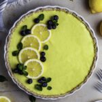 Vegan lemon pie in a white pie dish topped with lemon slices, blueberries, and fresh mint leaves.