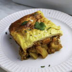 A piece of vegetarian Bulgarian moussaka topped with cilantro on a white plate.