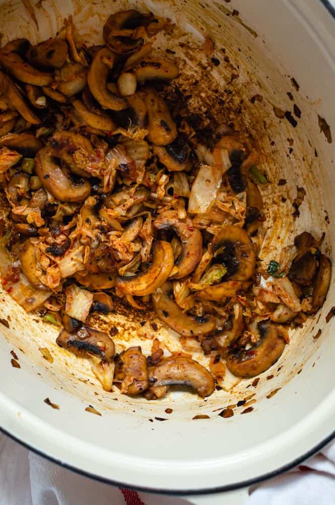 Cooked mushrooms, onion and kimchi in a white dutch oven.