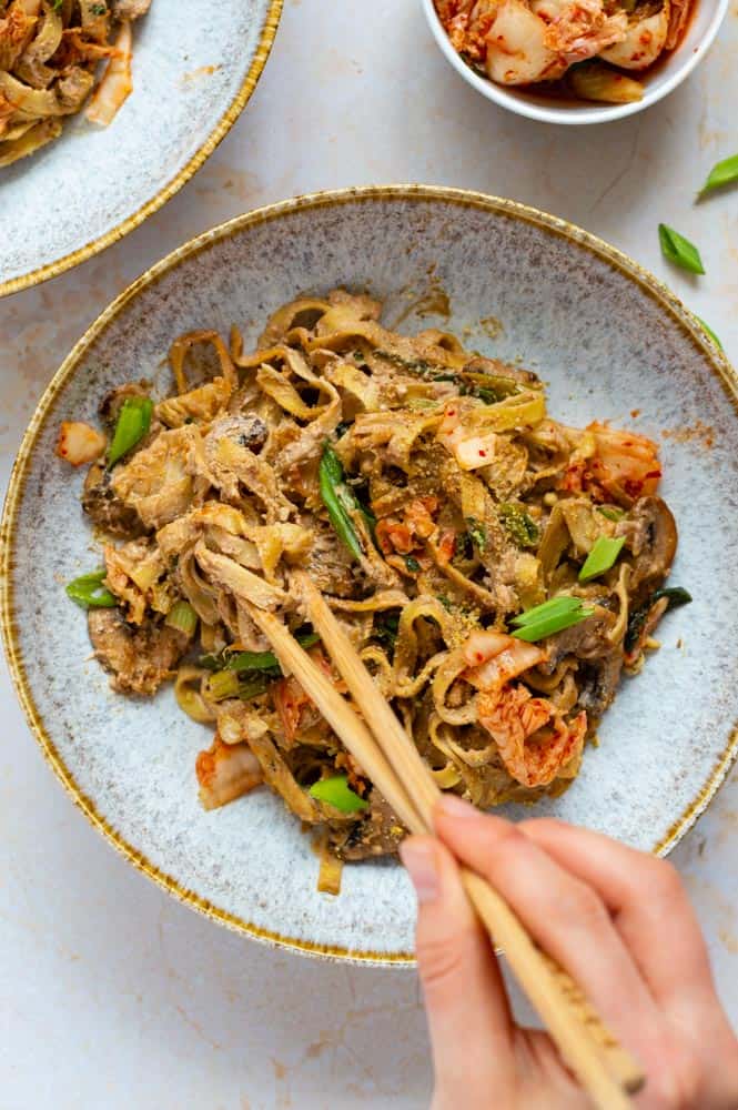 Stirring vegan alfredo fettuccine pasta with wooden chopsticks, in a blue bowl.