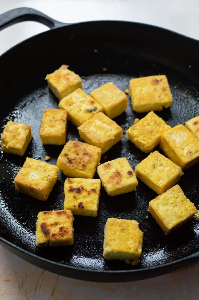 Cubed tofu frying in a black cast iron skillet. The tofu is crispy and lightly golden.