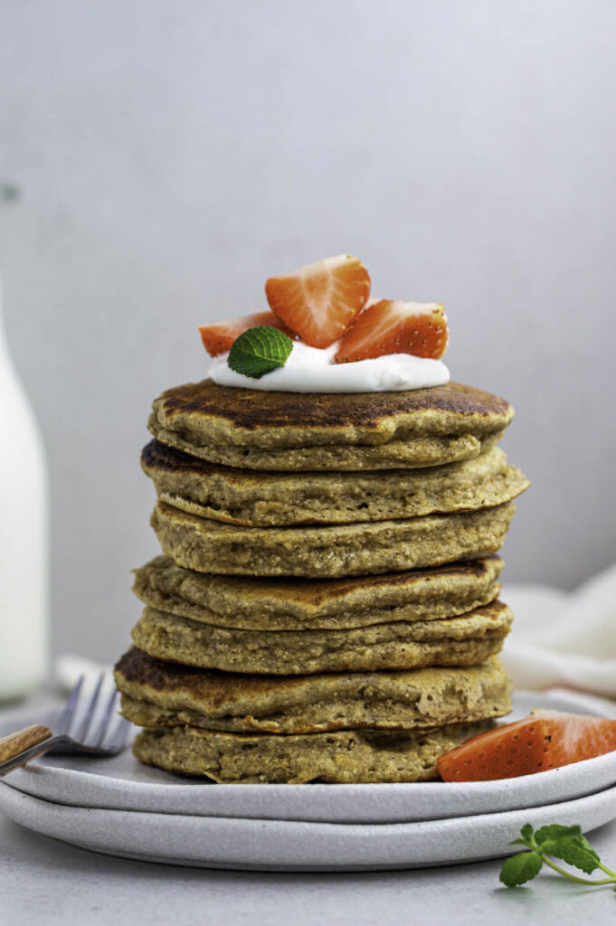 A stack of banana oat pancakes topped with yogurt, and strawberries.