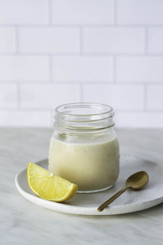 A jar filled with dressing for kale salad, a slice of lemon and a spoon placed next to it