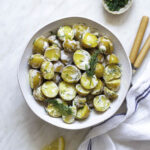 A white bowl filled with potato salad without eggs topped with chopped fresh dill.
