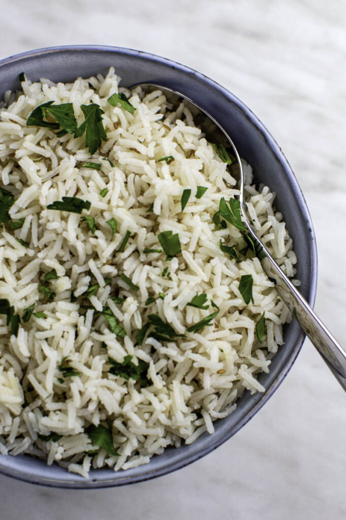 A close-up shot of coconut rice in a blue bowl, topped with chopped parsley