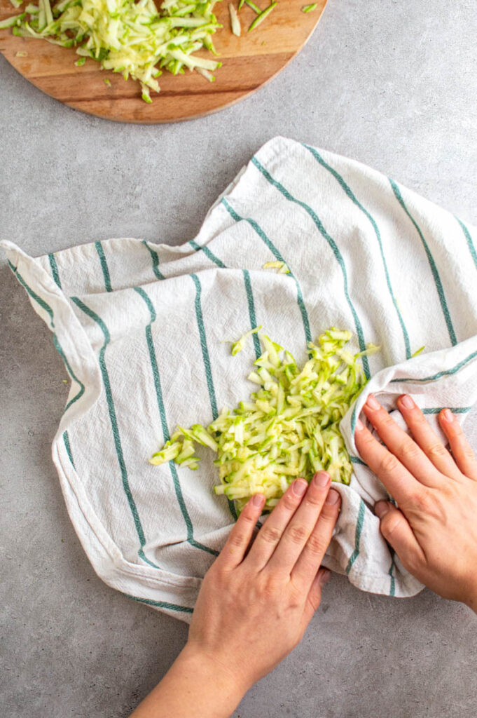 Two hands wrapping shredded zucchini in a kitchen towel