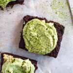 A piece of zucchini brownie on a piece of parchment paper topped with cashew matcha frosting.