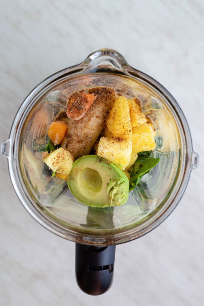 A glass blender jar filled with ingredients for making spinach avocado smoothie.