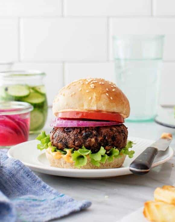 Black bean burger served in a white plate with a knife next to it.