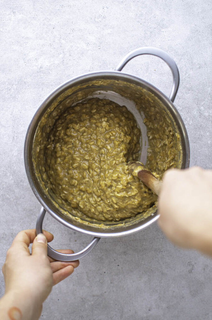 Stirring oatmeal with a wooden spoon, in a stainless steel pot