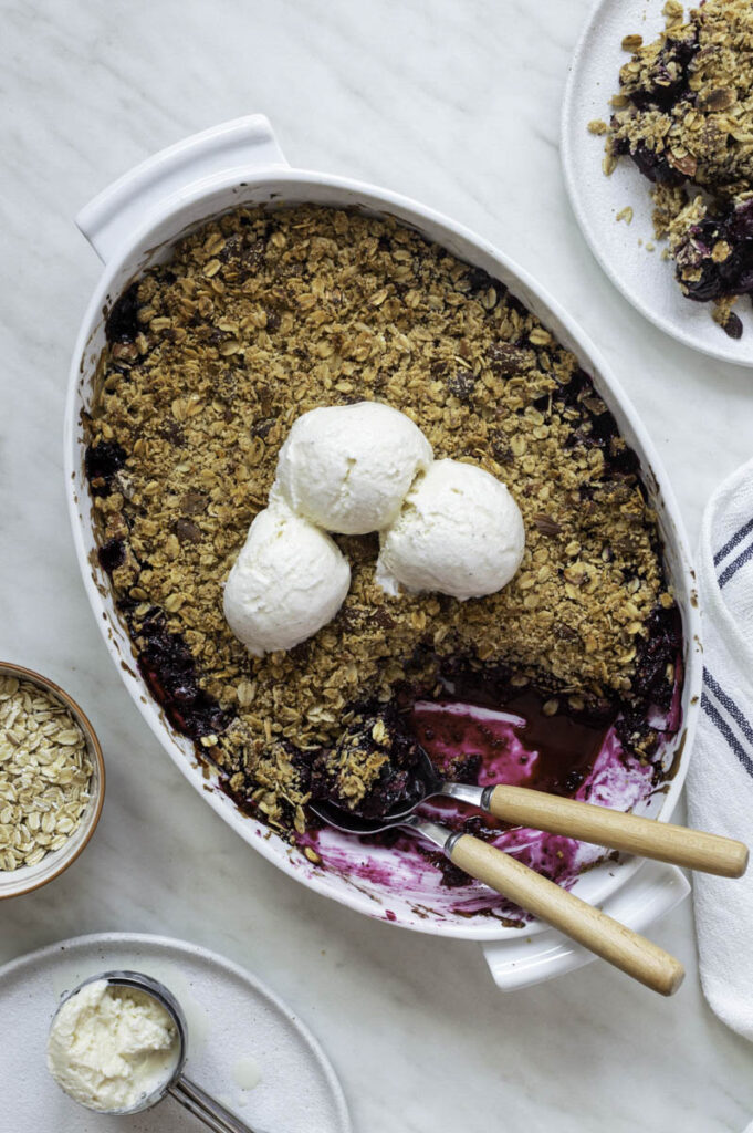 Blueberry crisp in a white baking dish, topped with 3 soups of ice cream