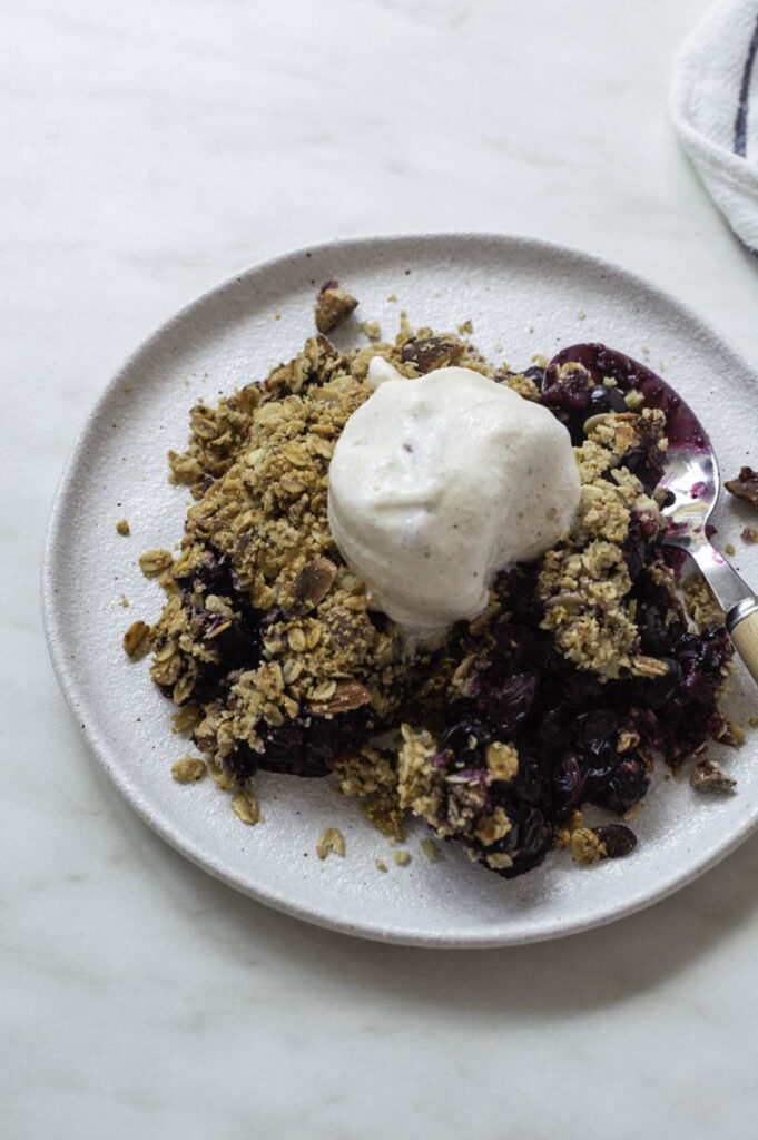 Blueberry crisp in a white plate, topped with a scoop of ice cream