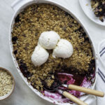 Berry crisp in a white casserole dish topped with three scoop of vanilla ice cream.