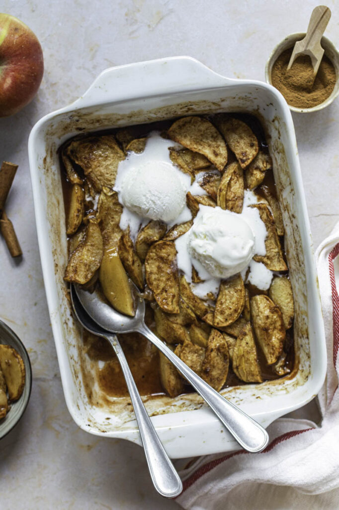 Ceramic baking dish filled with baked apples with cinnamon and topped with ice cream