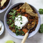 Dutch oven chili served in a blue bowl, topped with sour cream and chopped parsley