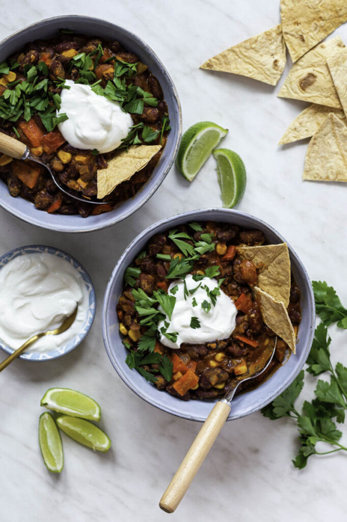 Two blue bowls, filled with chili and topped with sour cream and parsley