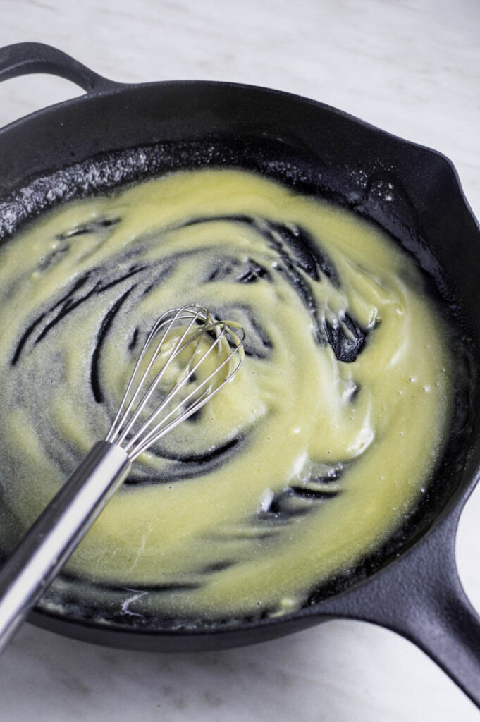 Whisking butter and flour in a cast iron skillet to make roux.