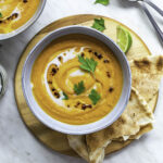Sweet potato soup served in a blue bowl, placed on a round wooden chopping board.