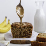 Pouring peanut butter with a spoon onto banana bread.