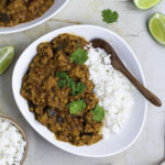 A white bowl filled with eggplant lentil curry and white rice.