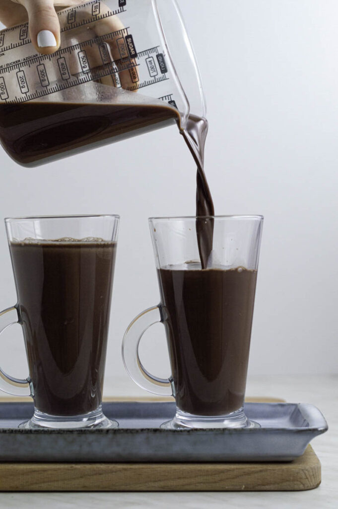 Pouring hot chocolate into a clear glass.