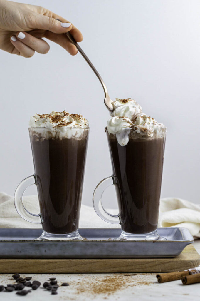 Scooping whipped cream from a glass filled with oat milk hot chocolate.