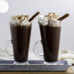 Two glasses filled with hot chocolate, and topped with whipped cream and ground cinnamon.