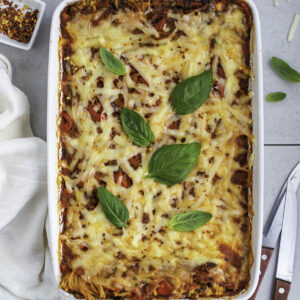 Vegan baked spaghetti in a white casserole topped with fresh basil leaves.