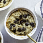 Chocolate chip cookie in a white mug with a golden spoon dipped in it.