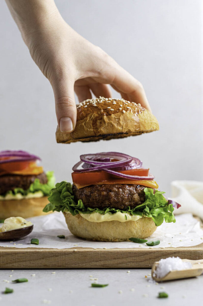 A hand placing the top bun on the Beyond burger.