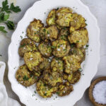 Crispy smashed potatoes on a white platter topped with chopped parsley and flaky sea salt.