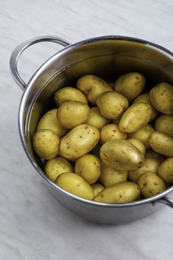Baby potatoes in a stainless steel pot filled with water.