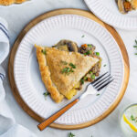 A piece of lentil pot pie served on a white plate, placed on a round wooden cutting board.