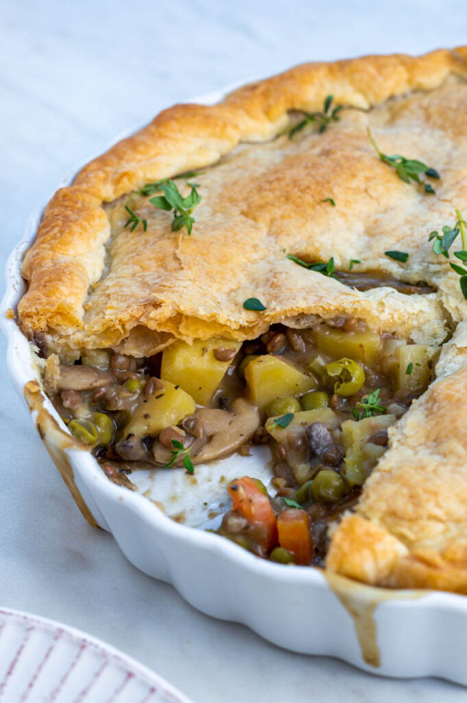 Lentil pot pie in a ceramic pie pan, garnished with fresh thyme on top.