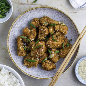 A blue bowl filled with teriyaki cauliflower wings, topped with sesame seeds and green onion.