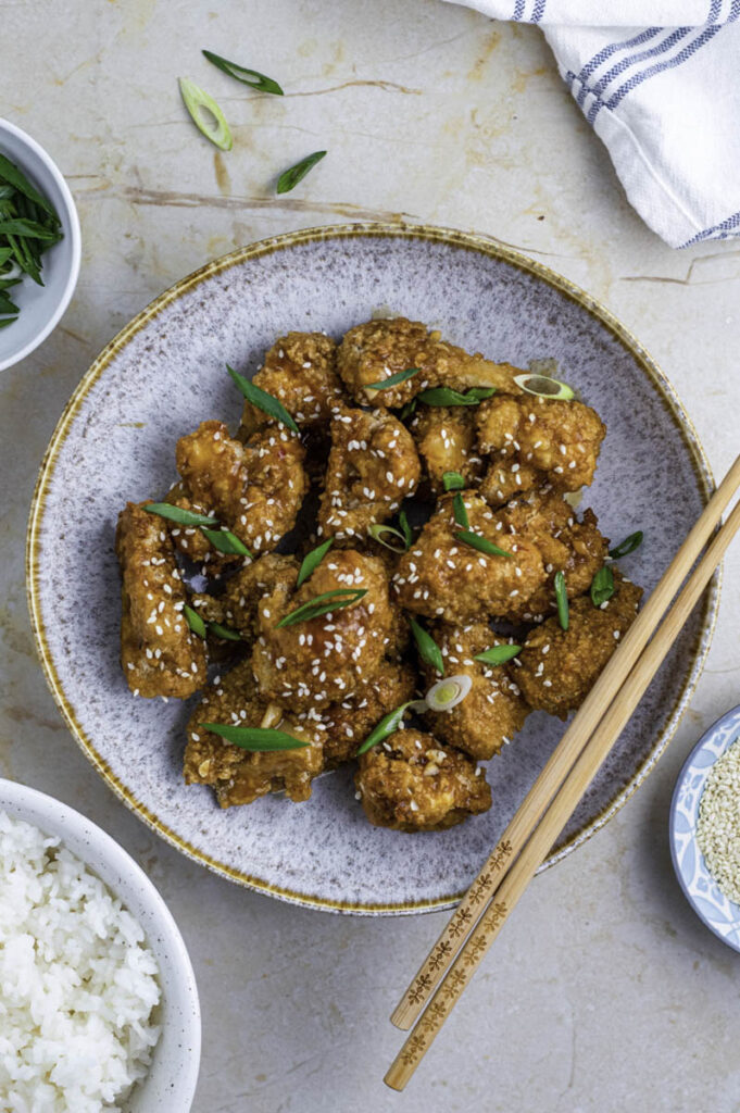 A blue bowl filled with teriyaki cauliflower wings, topped with sesame seeds and green onion.