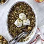 Apple crisp in a baking dish, topped with 3 scoops of yogurt and crushed walnuts.