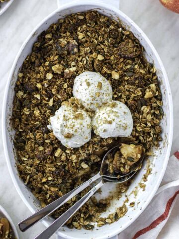 Apple crisp in a baking dish, topped with 3 scoops of yogurt and crushed walnuts.