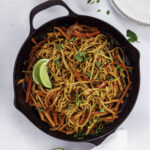 Garlic chili oil noodles in a black cast-iron skillet topped with cilantro.