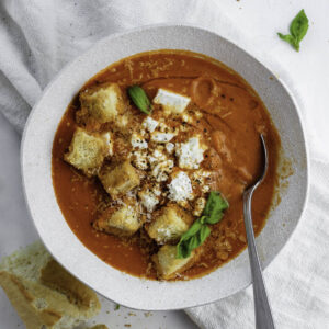 A white bowl filled with Mediterranean Tomato Soup topped with feta cheese and croutons.