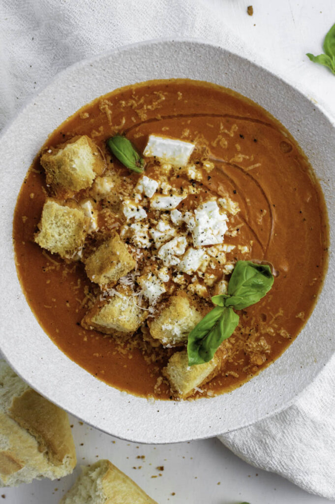 Mediterranean tomato soup served in a white bowl and topped with fresh basil, feta cheese and croutons.