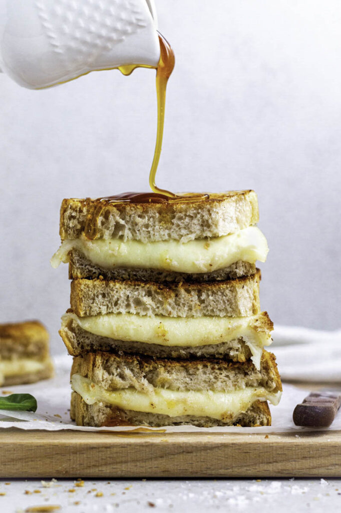 Pouring honey over a stack of provolone grilled cheese sandwiches.