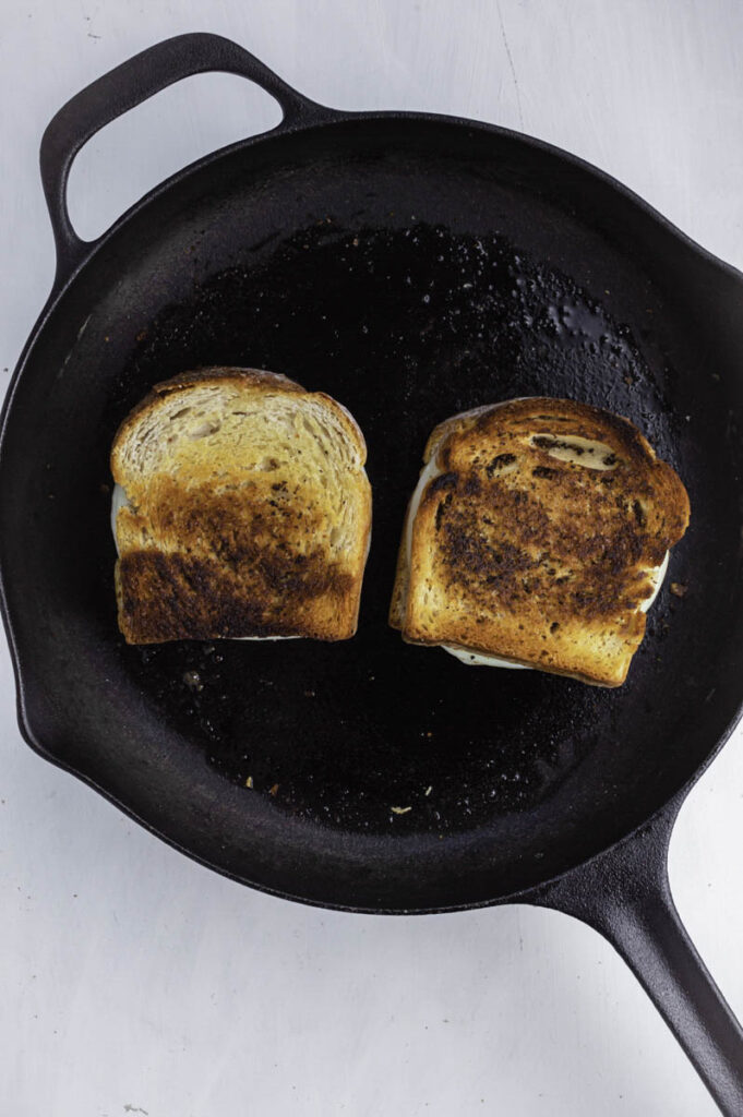 Grilled cheese sandiwches cooking in a black cast iron skillet.