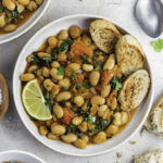 Spicy white bean stew served in a white bowl with sliced bread on the side.